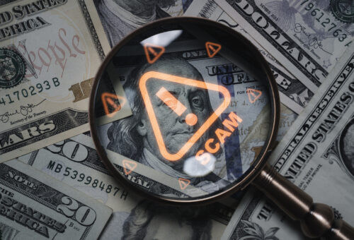 Magnifying glass focusing on scam warning symbol over dollar bills concept of financial fraud money laundering cybercrime and online scam alert for security awareness and finance protection