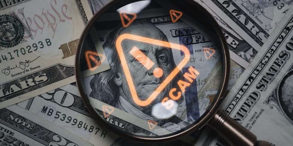 Magnifying glass focusing on scam warning symbol over dollar bills concept of financial fraud money laundering cybercrime and online scam alert for security awareness and finance protection